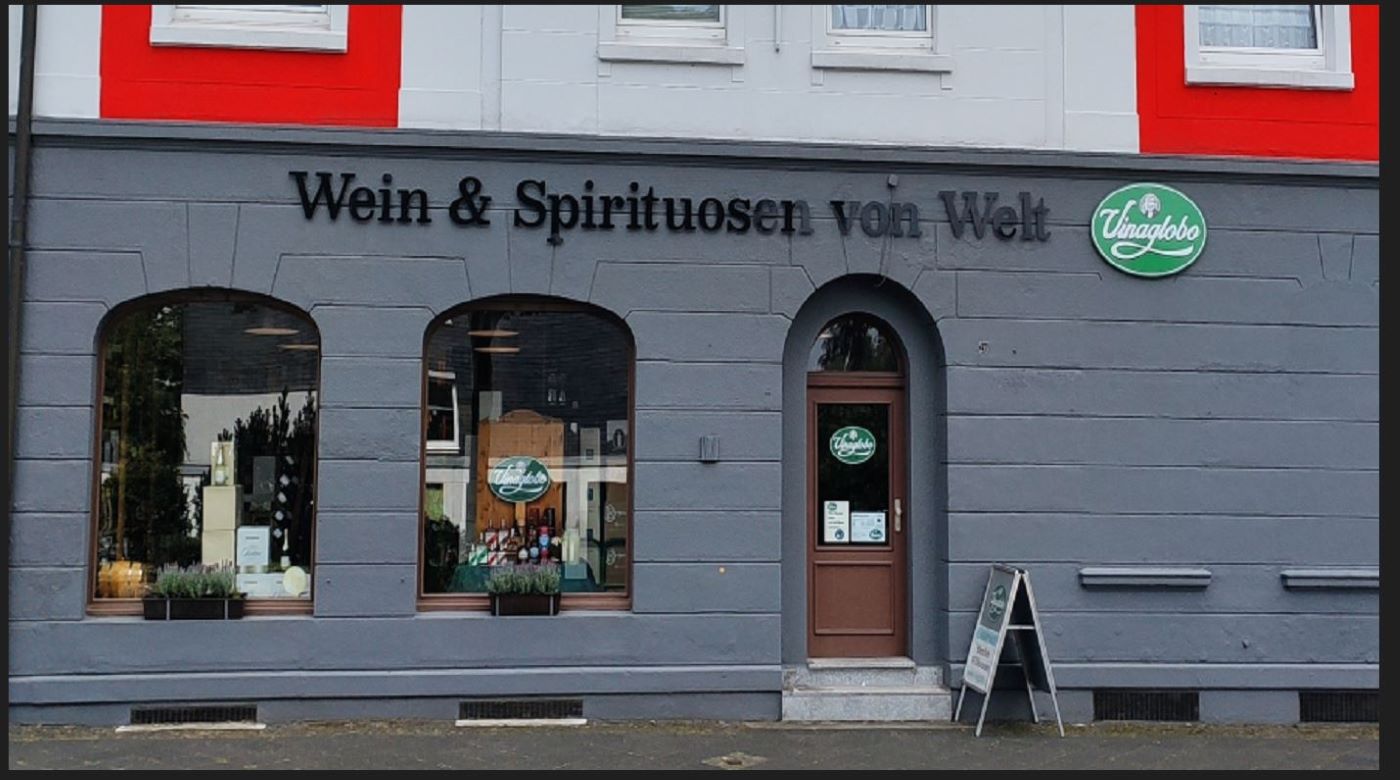 Graues Fachgeschäft mit Aufschrift „Wein & Spirituosen von Welt“ und Eingang.
