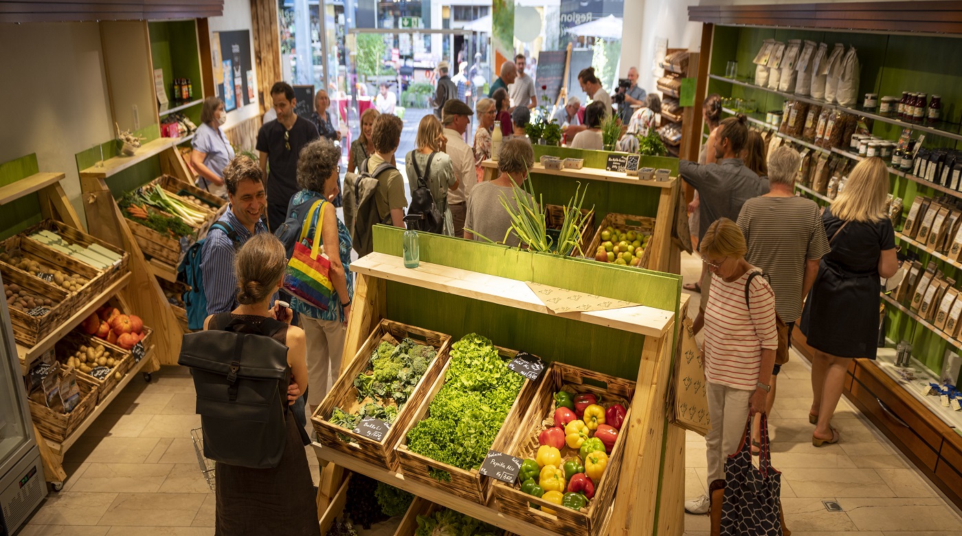Kunden kaufen frisches Gemüse und Obst in einem belebten Bioladen.