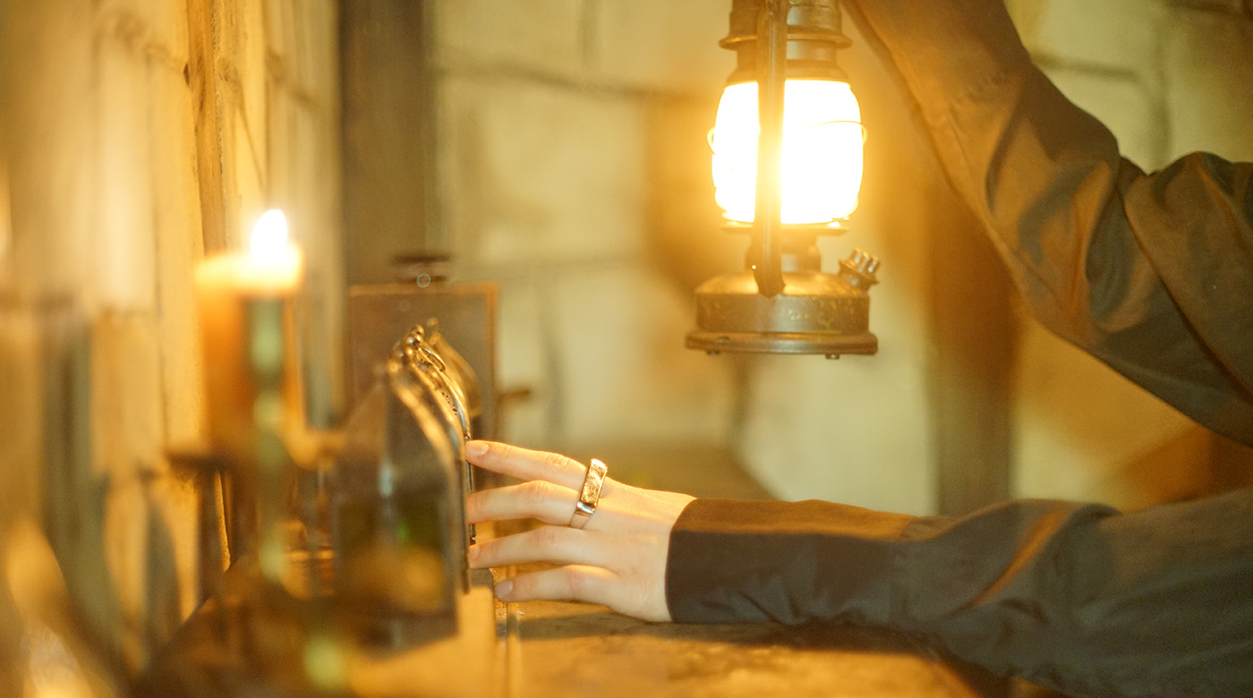 Hand betätigt Hebel in mystischer Umgebung, beleuchtet von Kerze und alter Laterne.