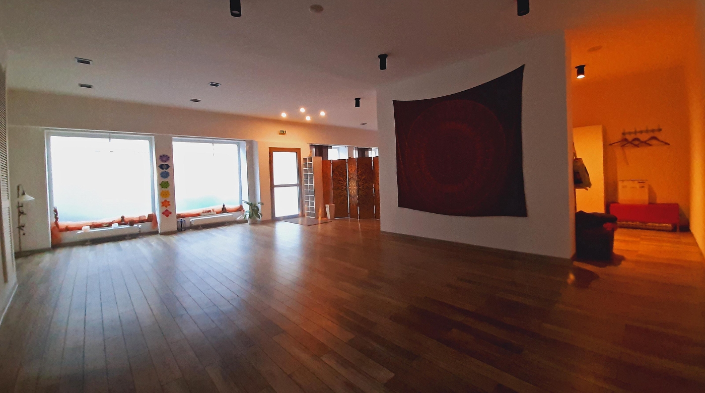 Heller Yoga-Raum mit Holzboden, großen Fenstern, Wandteppich und Raumtrenner.