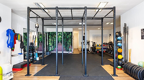 Heller Fitnessraum mit schwarzem Trainingsgerüst und Sportgeräten.